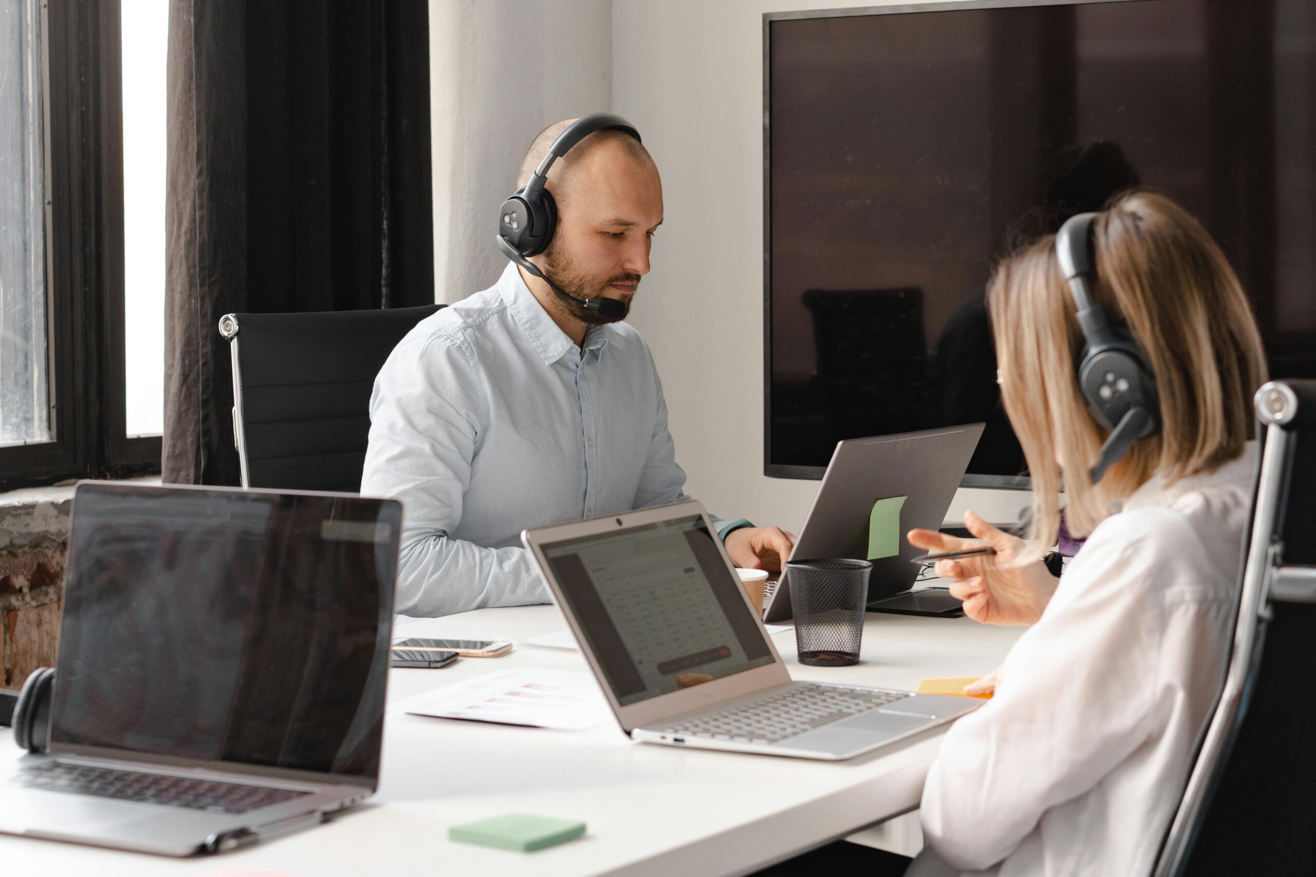 Happy man in office wearing headset, giving a thumbs up while typing at a computer.